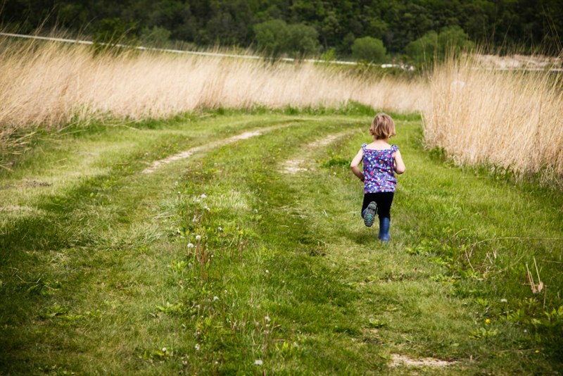 Child running along a grassy path in a natural setting, surrounded by tall grass and trees, capturing the essence of outdoor play and exploration.
