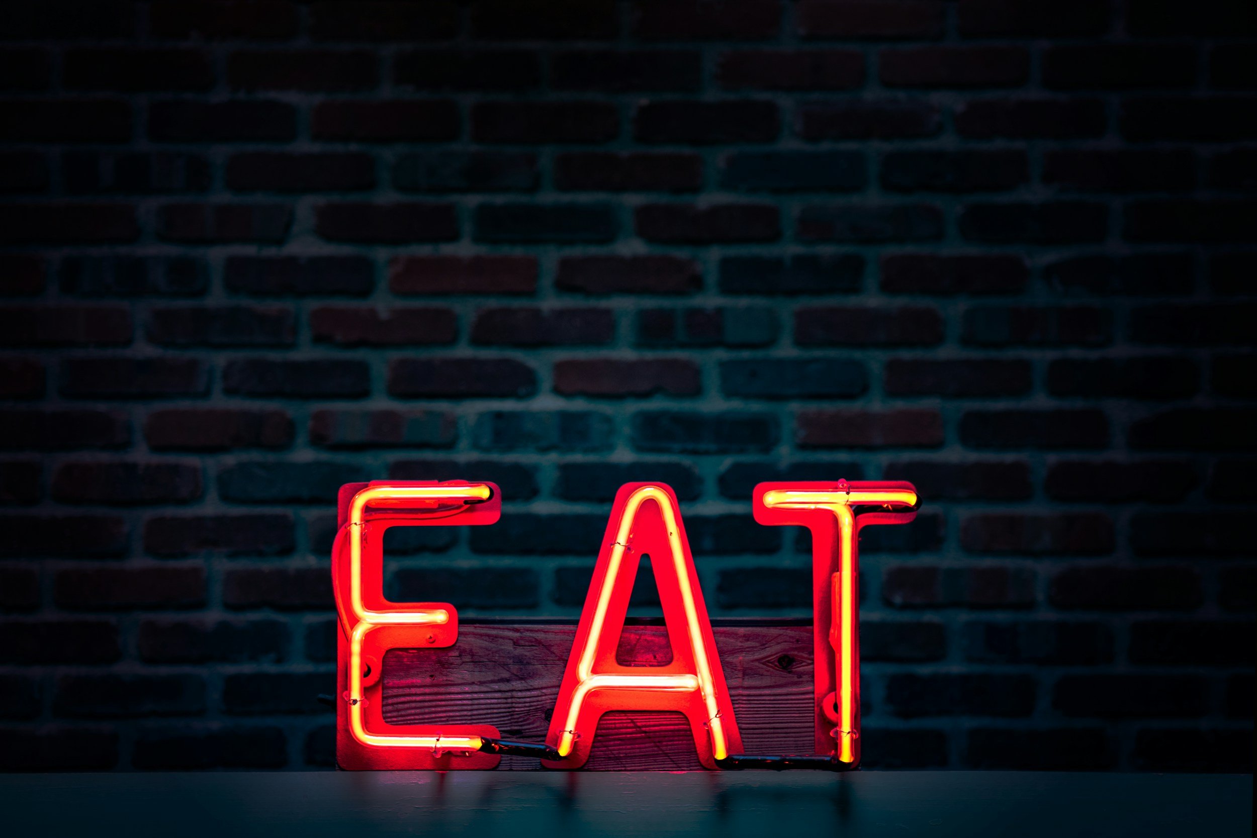 unsplash-image-FH3nWjvia-U Neon sign spelling "EAT" in bright red against a dark brick wall, creating an inviting atmosphere for dining and food-related themes.